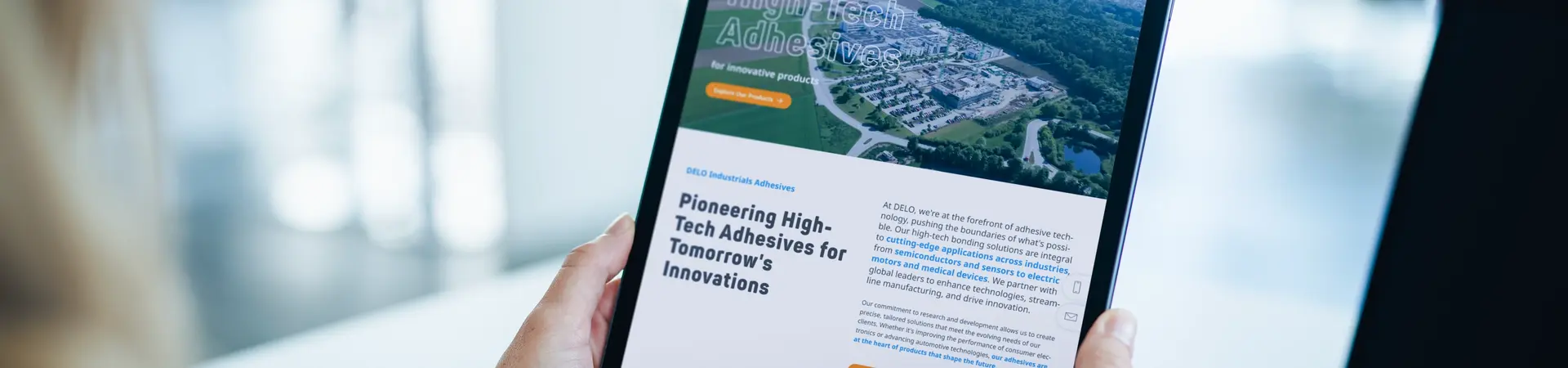 Tablet displaying DELO website for high-tech adhesives, showcasing innovative solutions for tomorrow. Person in white sweater holding device in front of laptop. Focus on pioneering adhesive technology for future applications. SEO-optimized presentation of DELO's expertise and global presence in advanced adhesives sector.